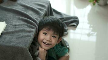 An Asian boy is playing hide and seek in a blanket table in his house. video