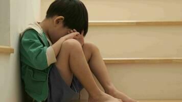 A sad Asian boy sits with his head down on the steps. video