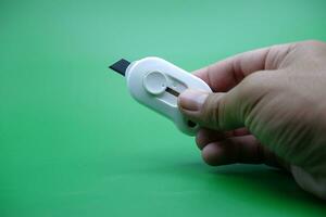 hand holding a white cutter isolated on a green background. photo