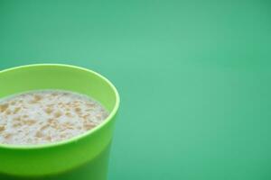 Green plastic cup containing cereal drink isolated on green background photo