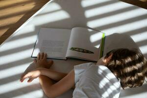 un niño tendido en un cama leyendo un libro foto