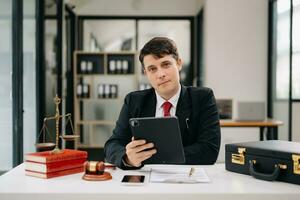 justicia y ley concepto. masculino juez en un sala de justicia el mazo, trabajando con inteligente teléfono y ordenador portátil y digital tableta computadora en madera mesa foto