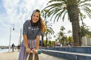 Portrait of happy teenage girl with skateboard on a promenade with palms photo