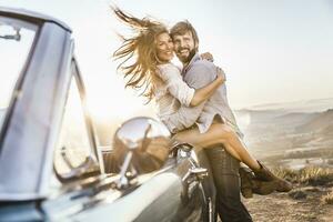 Happy couple at convertible car in the countryside at sunset photo