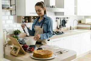 Young woman preparing a cream cake, using tablet photo