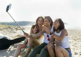 contento hembra amigos con cerveza botellas tomando un selfie en el playa foto