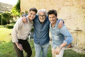 retrato de Tres contento hombres de diferente años abrazando en jardín foto