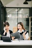 Two Asian business workers talking on the smartphone and using laptop at the modern office. photo