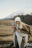 UK, Scotland, happy young woman carrying friend piggyback in rural landscape photo
