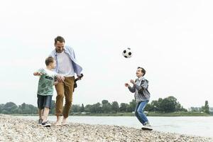 Happy father with two sons and football walking at the riverside photo