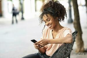 Smiling young woman sitting on a bench using cell phone photo