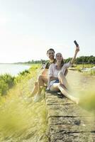 contento Pareja a el orilla en verano tomando un selfie foto