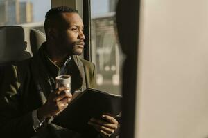 Portrait of stylish businessman with reusable cup and documents inside a train photo