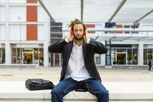 Portrait of young businessman with dreadlocks listening music with headphones and cell phone photo