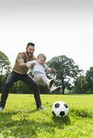 Happy father playing football with son in a park photo