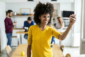 Happy woman taking a selfie at home with friends in background photo