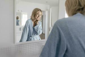 retrato de sonriente maduro mujer mirando en baño espejo foto