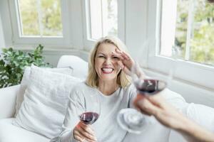 Portrait of laughing blond mature woman toasting with red wine at home photo