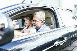 pequeño niña sentado en regazo de abuelo, fingiendo a dirigir el coche foto