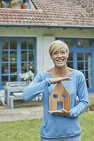 Portrait of smiling woman standing in front of her home holding house model photo