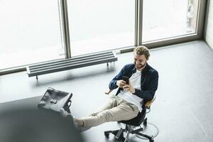 Smiling casual businessman sitting in office with feet up using cell phone photo