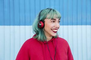 retrato de riendo joven mujer con azul teñido pelo escuchando música con auriculares foto