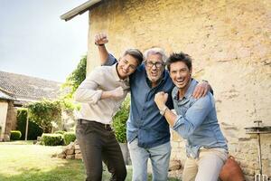 Portrait of three excited men of different age embracing and cheering in garden photo
