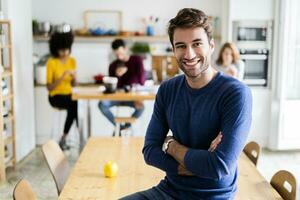 Portrait of smiling man at dining table at home with friends in background photo