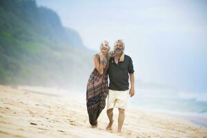 Happy senior hippie couple strolling side by side on the beach photo