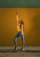 Teenage girl dancing with hand raised against yellow wall on street photo