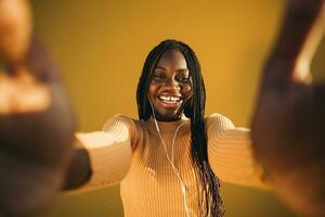 Happy teenage girl taking selfie while listening music against yellow wall photo