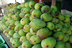 pile of mangoes on a wooden shelf for sale at a traditional market photo