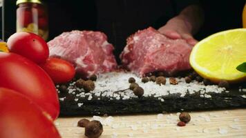 chef toepassen korrelig zout Aan rauw stuk van steak. kookplaat voorbereidingen treffen vlees Aan professioneel keuken tafel met divers groenten 4k beeldmateriaal video