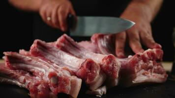 The chef cuts raw meat ribs with a knife in slow motion. Raw beef steak sliced on a wooden board. Delicious food concept video