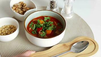 Traditional Hungarian dish, goulash, slow-cooked with beef, potatoes, carrot, tomatoes, paprika, onion and bell peppers. White bowl on wooden table. video