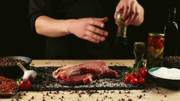 chef appliquant à grain sel sur brut pièce de steak. cuisinier en train de préparer Viande sur professionnel cuisine table avec divers des légumes 4k métrage video