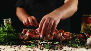 chef toepassen korrelig zout Aan rauw stuk van steak. kookplaat voorbereidingen treffen vlees Aan professioneel keuken tafel met divers groenten 4k beeldmateriaal video