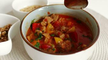 Traditional Hungarian dish, goulash, slow-cooked with beef, potatoes, carrot, tomatoes, paprika, onion and bell peppers. White bowl on wooden table. video