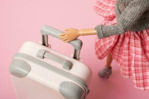 The doll carries a suitcase on wheels. Travel, vacation creative minimalistic concept photo