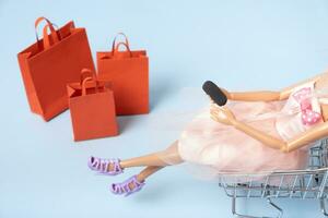 Doll in supermarket basket with smartphone and shopping bags top view. Sale concept photo