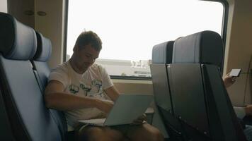 Visualizza di giovane uomo seduta nel il treno e utilizzando il computer portatile contro finestra durante viaggio, Olanda video