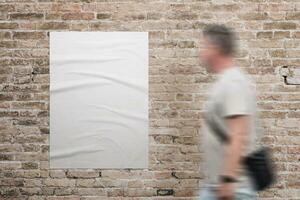 Wrinkled, blank A3 poster in white, adhered to a brick wall. A man walks beside. Ad or marketing campaign design promotion photo