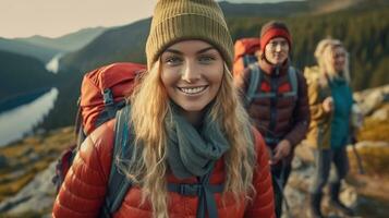 un sonriente joven mujer caminante con mochila mirando a cámara con grupo de amigos caminantes sube a el parte superior de el colina. caminante, turista acampar. generativo ai foto