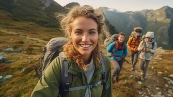 un sonriente joven mujer caminante con mochila mirando a cámara con grupo de amigos caminantes sube a el parte superior de el colina. caminante, turista acampar. generativo ai foto