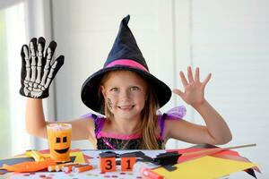 A little girl in a witch costume looks at the camera and laughs, holding a skeleton glove. photo