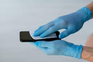 Close up is for men is hands in medical  rubber gloves to rub a mobile phone screen with a napkin. photo