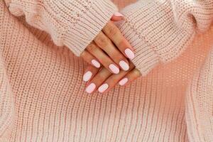 hembra manos con hermosa de forma ovalada clavos, mate rosado manicura de cerca en un rosado de punto suéter antecedentes. goma laca. foto