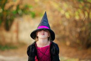 A portrait of a little girl in a witch costume hiding behind a black cap and showing her tongue. Halloween holiday. photo