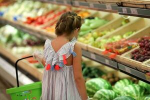 A girl in a medical mask in a supermarket buys vegetables and fruits. photo