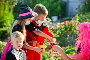 Children trick or treat in Halloween costume and medical mask. A little boy, girl and baby in suits during the coronavirus pandemic receive candy from a woman . photo